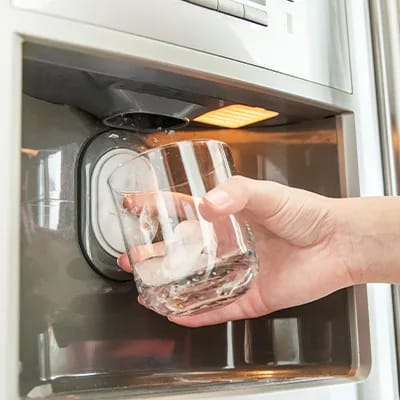 Hand holds glass and uses refrigerator water dispenser