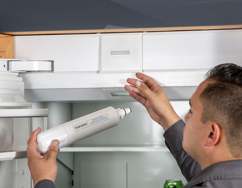 Appliance service technician replaces water filter on refrigerator